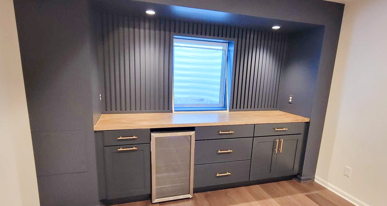 A wetbar frames an egress window. The wetbar features drawer and cabinet storage with a butcher block topper. 